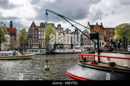 Amsterdam, Niederlande - 27 April 2017: Cruise touristische Boot gegen Hausboote, Bargen und typische Kurven niederländischen Häusern mit großen Fenstern in B Stockfoto