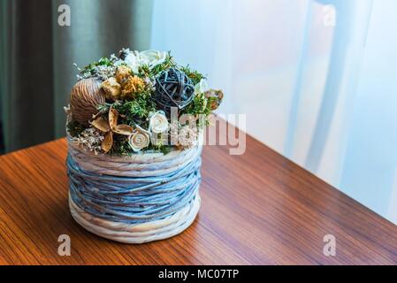 Nahaufnahme eines Wicker Blumentopf mit getrockneten Blumen Anordnung über einen hölzernen Tisch am Fenster. Stockfoto