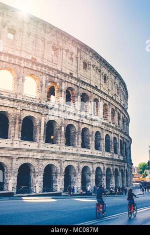 Rom, Italien, 24. April 2017. Seitliche Sicht auf das Kolosseum/Colosseo/Amphitheater mit Touristen zu Fuß oder mit dem Fahrrad entlang der Via dei Fori Imperiali Stockfoto