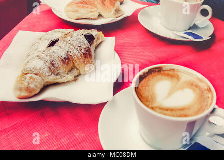 Frühstück in einem italienischen Restaurant - ein Croissant und eine Tasse Kaffee mit einem Herz aus Schaumstoff. Stockfoto