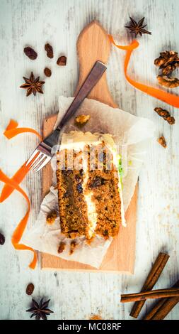 Blick von oben auf ein hausgemachter Karottenkuchen mit Rosinen, Nüssen und Zimt über weiß Holz- Hintergrund. Cream Cheese frosting. Stockfoto