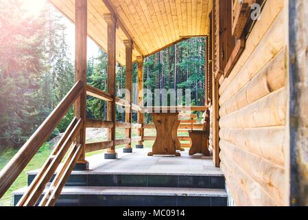 Seitenansicht eines offenen Veranda vor einem hölzernen Wald Ferienhaus. Kiefernwald unter den Strahlen der Sonne im Hintergrund Stockfoto