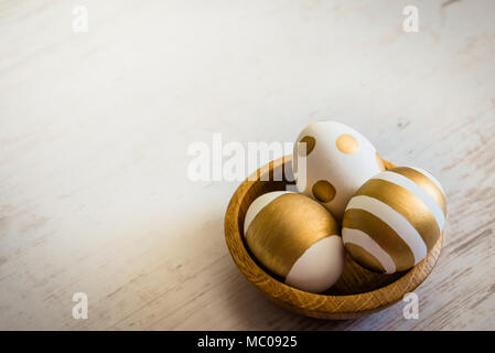 Nahaufnahme von Ostern Eier gefärbt mit goldenen Farbe in eine hölzerne Platte. Verschiedene gestreifte und gepunkteten Designs. Weiß Holz- Hintergrund. Stockfoto