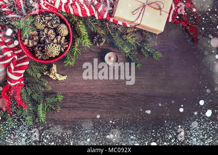 Blick von oben auf die weihnachtsdekoration - rot Schüssel voller Fir-Kegel, Geschenkbox in braunes Packpapier eingewickelt, Goldener Engel, Kiefer Äste, Kerze, Rot und Weiß Stockfoto