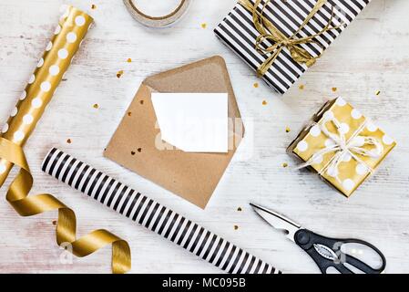 Leere Grußkarte in einem Handwerk Umschlag, Geschenkboxen und Verpackungsmaterial auf weißem Holz Hintergrund. Stockfoto