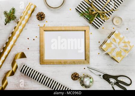 Golden ptoto Frame, Geschenkboxen, Tannenzapfen und Weihnachten Spielzeug und Verpackungsmaterial auf weißem Holz alt Hintergrund. Weihnachten Konzept. Frame mock up. Stockfoto