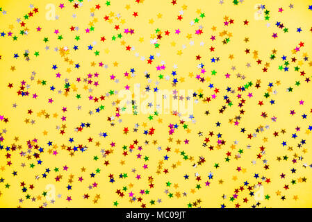 Zerstreut sternförmigen bunt glitzernden Konfetti auf gelben Hintergrund. Stockfoto