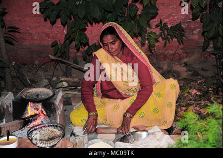 Portrait einer indischen Frau in farbenfrohem gelb Sari, Kochen paratha Brot auf einem traditionellen Holzofen Kaminofen (chulha) Stockfoto