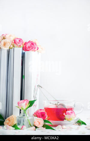 Bücherregal mit weißen Bücher, Rosen und einer Tasse Kräutertee. Romantische Freizeitaktivitäten und lesen Konzept auf einen weißen Hintergrund mit kopieren. Stockfoto