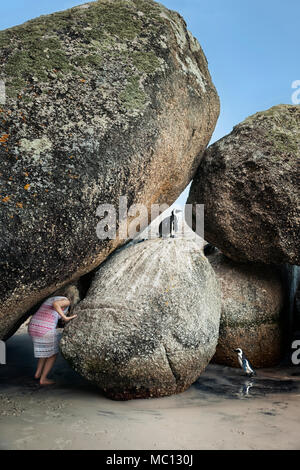 Model Released Frau Hockend zwischen riesigen Felsbrocken am Strand mit afrikanischen Pinguine Boulders Beach National Park, Simonstown, Südafrika Stockfoto