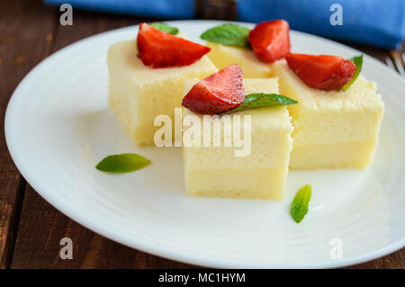 Feine Hüttenkäse und cremig Souffle in Form von Würfeln, Verzieren mit Minze und frischen Erdbeeren auf einem weißen Teller. Nahaufnahme Stockfoto