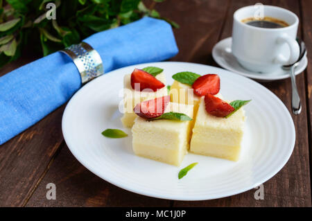 Feine Hüttenkäse und cremig Souffle in Form von Würfeln, Verzieren mit Minze und frischen Erdbeeren auf einer weißen Platte Stockfoto