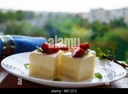 Feine Hüttenkäse und cremig Souffle in Form von Würfeln, Verzieren mit Minze und frischen Erdbeeren auf einem weißen Teller auf einem Hintergrund o Stockfoto