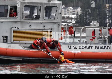 Mitglieder der Coast Guard Station Juneau ein Dummy ziehen aus dem Wasser beim Leiten der Mann über Bord Ausbildung in Juneau, Alaska, Jan. 24, 2018. Station Juneau durchgeführt, um die Mann-über-Bord-Position Bohrer bei Frost zu erhalten neue Mitglieder boatcrew qualifiziert. U.S. Coast Guard Foto von Petty Officer 1st Class Jon-Paul Rios. Stockfoto