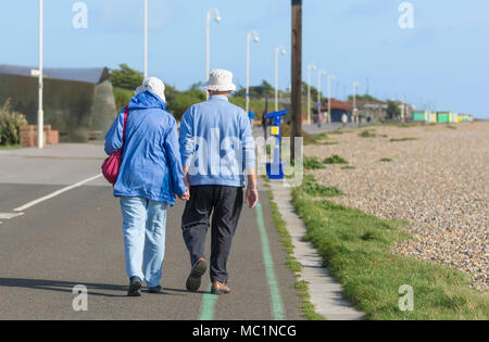 Senior Paar entfernt halten sich an den Händen entlang der Strandpromenade, an einem sonnigen Tag in Littlehampton, West Sussex, England, UK. Direkt am Meer spazieren. Stockfoto