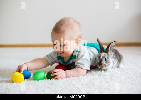 Wenig Kleinkind Kind, baby boy, spielen mit Hasen und Ostereier zu Hause, bunte hand Zeichnungen auf den Eiern Stockfoto