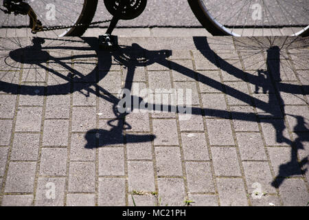 Ein geparktes Fahrrad wirft einen Schatten auf dem Bürgersteig. Stockfoto