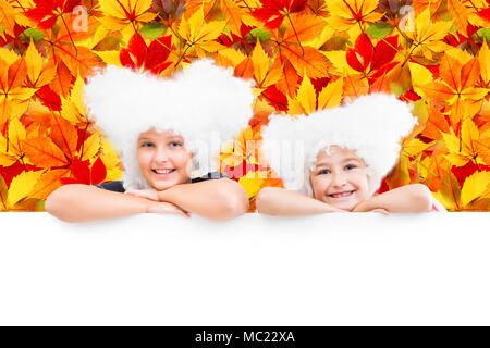 Lächelnd glücklich zwei junge Mädchen in weißen Perücken schauen Sie heraus aus den leeren Banner auf dem Hintergrund der gefallenen Blätter im Herbst. Stockfoto