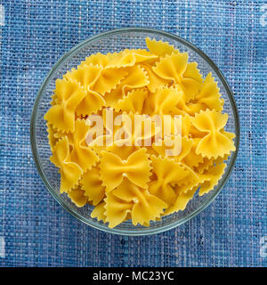 Farfalle Makkaroni Nudeln in eine Glasschüssel auf einem blauen Hintergrund in der Mitte gestrickt. Close-up mit der Spitze. Stockfoto