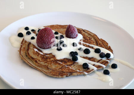 Frische, hausgemachte Pfannkuchen mit Joghurt und Blaubeeren und Erdbeeren serviert. Stockfoto