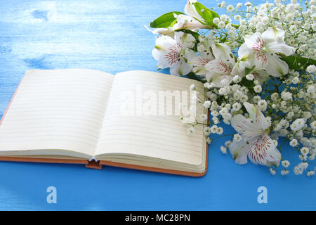 Blick von oben auf die weiße Blumen Anordnung und leeren öffnen Notebook über blau Holz- Hintergrund. Platz kopieren Stockfoto