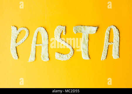 Das Wort "Pasta wird in umfangreichen Briefe von kleinen rohen Makkaroni auf gelbem Hintergrund gelegt. Essen auf einem hellen Hintergrund Stockfoto