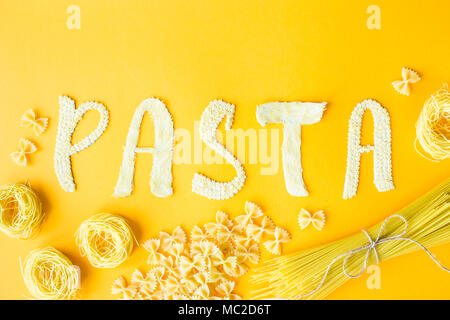 Das Wort "Pasta wird in Massen Briefe von kleinen rohen Makkaroni auf gelbem Hintergrund festgelegt sind neben einer Vielzahl von Arten von Pasta. Essen auf einem hellen backgr Stockfoto