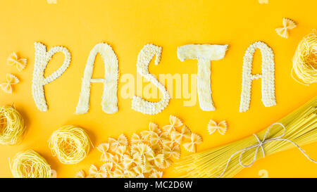 Das Wort "Pasta wird in Massen Briefe von kleinen rohen Makkaroni auf gelbem Hintergrund festgelegt sind neben einer Vielzahl von Arten von Pasta. Essen auf einem hellen backgr Stockfoto