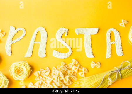 Das Wort "Pasta wird in Massen Briefe von kleinen rohen Makkaroni auf gelbem Hintergrund festgelegt sind neben einer Vielzahl von Arten von Pasta. Essen auf einem hellen backgr Stockfoto
