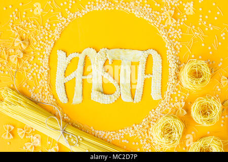 Das Wort "Pasta wird in umfangreichen Briefe von kleinen rohen Makkaroni in einem Kreis unter verschiedenen Arten von Nudeln. Essen auf einem hellen Hintergrund Stockfoto