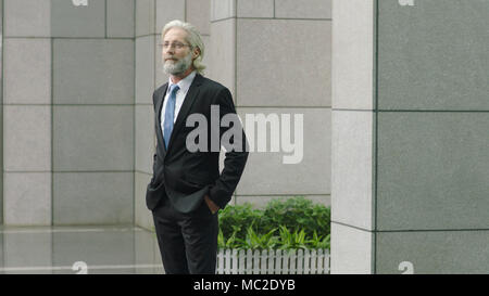 Kaukasische corporate Geschäftsmann ständigen Denken im Hof des modernen Gebäude, Hände in den Taschen. Stockfoto