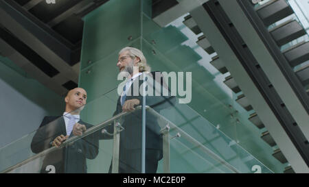 Zwei Führungskräfte stehen in der zweiten Etage eines modernen Bürogebäudes diskutieren. Stockfoto