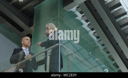 Zwei Führungskräfte stehen in der zweiten Etage eines modernen Bürogebäudes diskutieren. Stockfoto