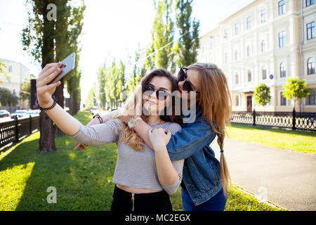 Outdoor Portraits von zwei hübschen Mädchen Freund unter selfie. schöne Blondine umarmen und gemeinsam Spaß haben. Verschleiß Sommer Sonnenbrille und machen Fotos, Der Stockfoto