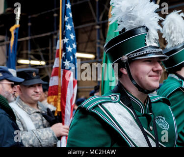 Lächelnd Brewster High School junge märschen in Band am St. Patrick's Day Parade, New York 2018. Grüne uniform, White Feather plume. Close Up. USA-Flagge. Stockfoto