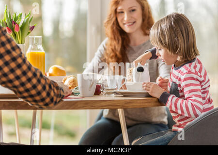 Junge gießen Milch in seine Schale beim Frühstück mit seinen Eltern Stockfoto