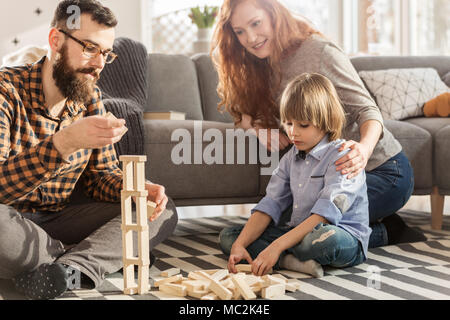 Junge Eltern spielen mit Holzblöcken mit ihrem Sohn in einem Wohnzimmer Stockfoto