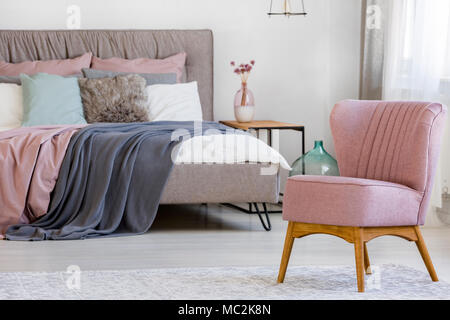 Nahaufnahme einer rosa Stuhl stehend in einem hellen Schlafzimmer mit Blumen auf einem Tisch Stockfoto