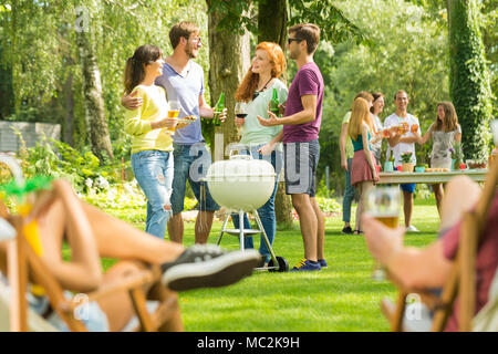 Gruppe von jungen Freunden sprechen, an einem sonnigen Tag, genießen Sommerferien Bier trinken und Grillen in der Natur Stockfoto