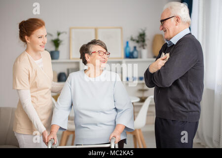 Lächelnd senior Paar und eine junge Krankenschwester helfen, die Frau zu Fuß Stockfoto