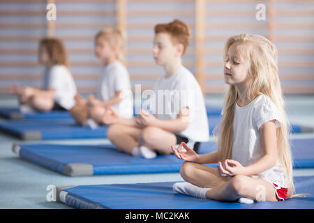 Gruppe von Kindern sitzt im Lotussitz auf blauen Matten während einer Yogastunde Stockfoto