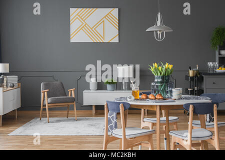 Elegante, weiße und goldene Kunstwerke und eine moderne Sessel in einer monochromatischen offenen Raum Apartment mit Wohn- und Essbereich Stockfoto