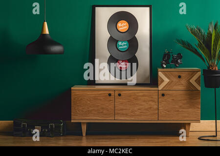 Palm Tree Pflanze in einem hohen pflanzmaschine Neben einem hölzernen, retro Sideboard in einem hipster Wohnzimmer Interieur mit Teal Green wall Stockfoto