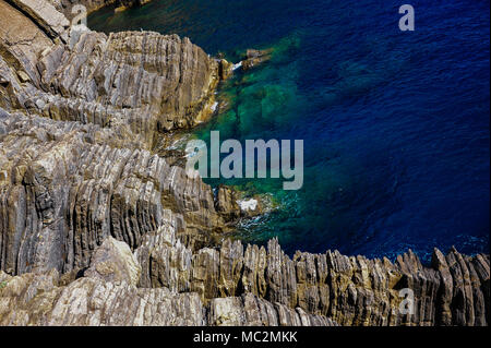 Via dell'Amore Manarola und Riomaggiore: Nahaufnahme, Detail der Streifen entlang der felsigen Ligurische Küste gegen deep blue sea Hintergrund gebildet Stockfoto