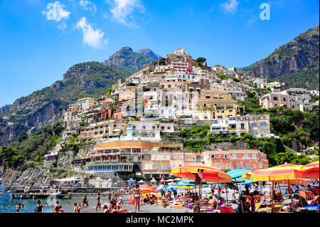 Bunte Szene am Strand Spiaggia Grande (Strand) in Positano, Italien. Urlauber entspannen unter Schirmen mit der Stadt aufragenden Stockfoto