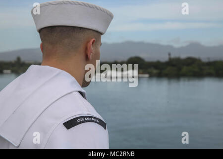 PEARL HARBOR NAVAL BASE, HI - ein Seemann mit dem Amerika Amphibious Ready Gruppe an Bord amphibisches Schiff USS America (LHA 6) die Schienen mans, wie sie das USS Arizona Memorial verlassen, Jan. 25, 2018. Manning der Schienen ist ein Naval Tradition jede Bereitstellung von Schiff führt und ist eine Methode der ehrenkompanie oder Rendering Ehren durch Marineschiffe verwendet. Die 15. MEU und Amerika ARG sind derzeit auf eine Routine für sieben Monate, um die Bereitstellung zu den USA 3., 5. und 7 Flotte Bereiche des Betriebes als Reaktion auf Krisen und Kontingenz Kraft eingesetzt. (U.S. Marine Corps Foto von Cpl. Timothy Valero) Stockfoto