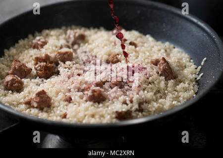 Nahaufnahme von einem vollen Topf mit Reis mit Würstchen und Rotwein, Chef ist Gießen Rotwein in der Pfanne beim Kochen italienische Risotto. Stockfoto