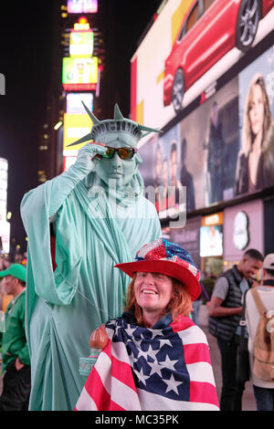 Lächelnde Frau in einer US-Flagge und Hut gesehen drapiert, gesehen posiert mit einem kostümierten street Entertainer wartet es Bild während der Abend berücksichtigt werden. Stockfoto