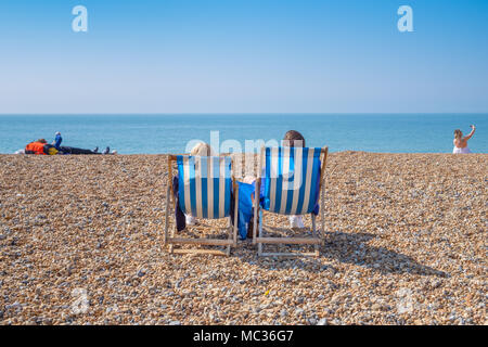 BRIGHTON, Großbritannien - 8 April 2017: Paar sitzen in Liegestühlen auf einem sonnigen April Tag auf Brighton Beach im April 2017.