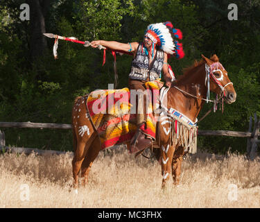 Krieger in Komantschen-Kleidung reitet Kastanienpferd, zeigt mit Speer, New Mexico Stockfoto